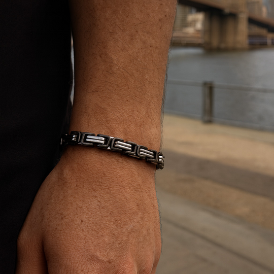 Close-up of a person's wrist wearing a black and silver bracelet with a blurred background.