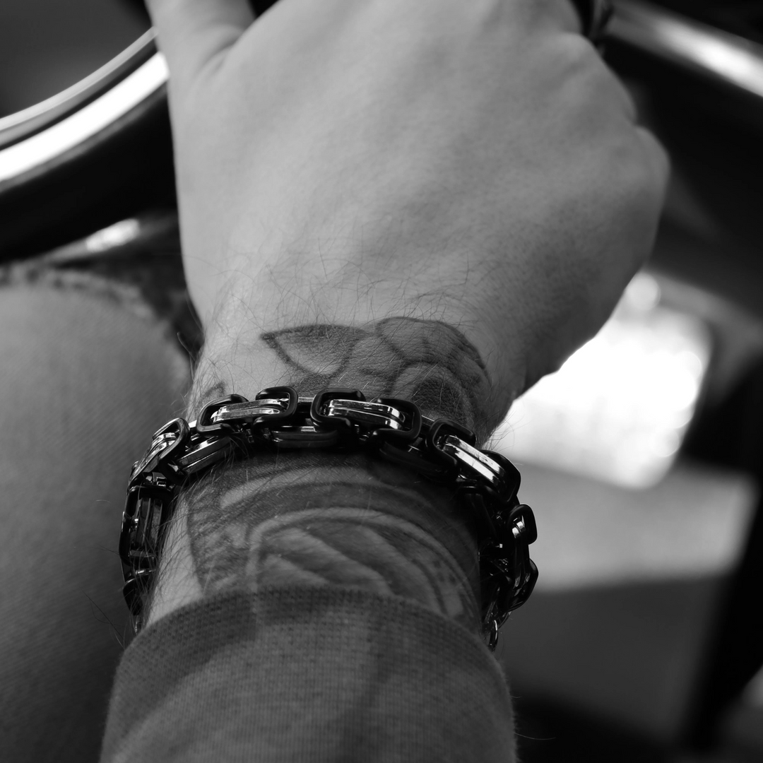 Black and steel bracelet on a wrist with tattoos, blurred background