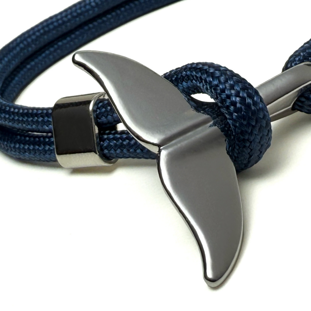 A close up image of a whale tail clasp on a blue rope bracelet 
