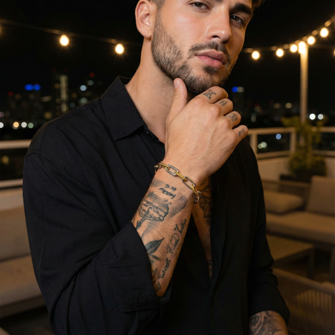 Man with tattoos wearing a black shirt in an outdoor evening setting, wearing a gold and steel bracelet