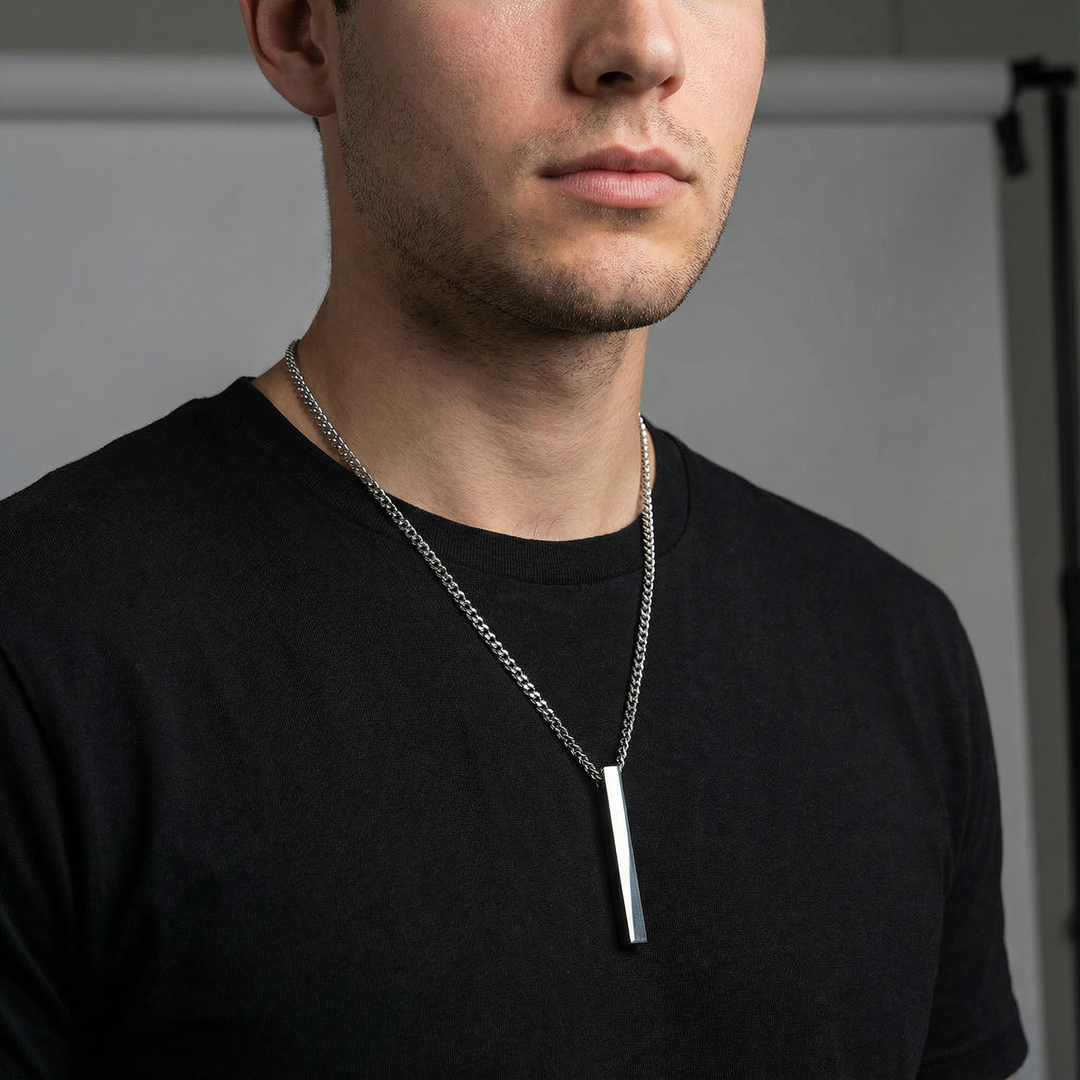 Man wearing a black shirt with a stainless steel necklace featuring a rectangular pendant.