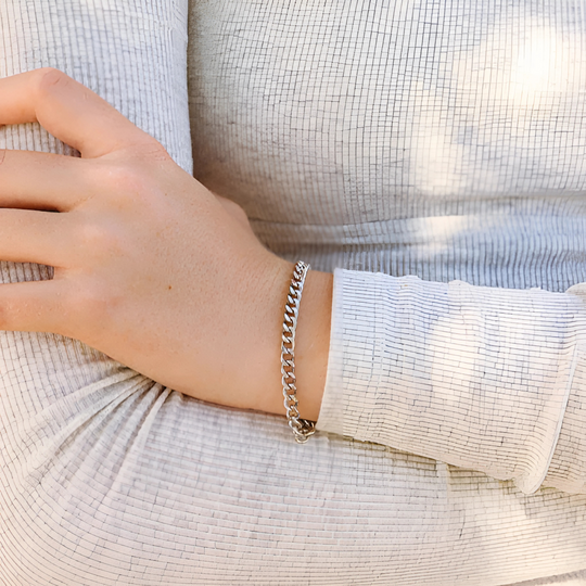 Hand wearing a stainless steel chain bracelet on a light fabric background