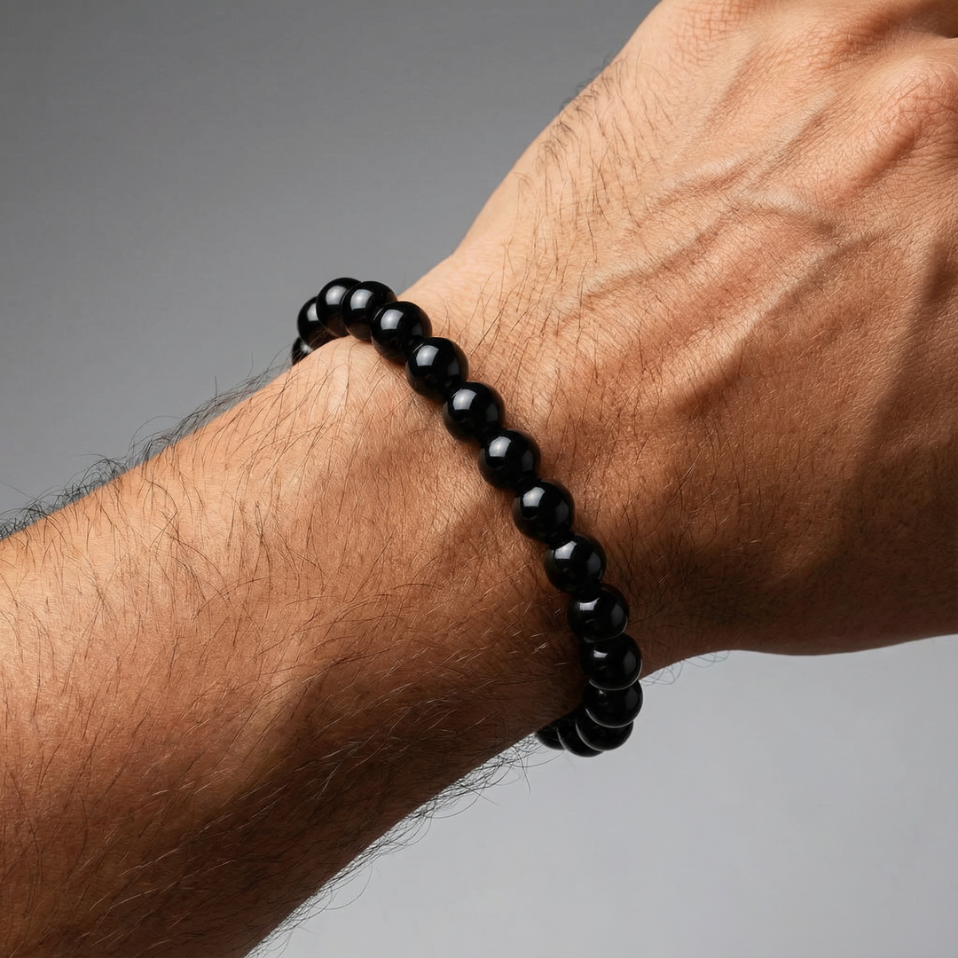 Black beaded bracelet on a wrist against a gray background