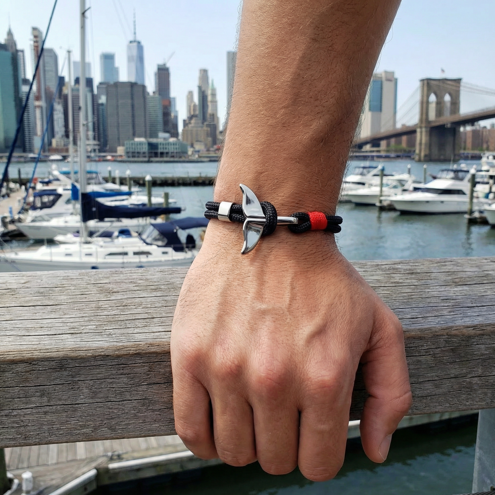 Hand wearing a bracelet with a unique design, set against a cityscape with boats and a bridge.