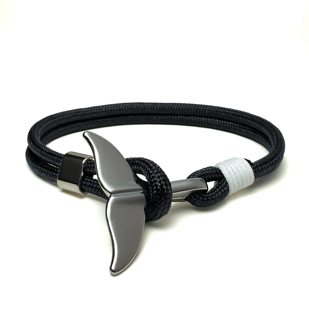 A bracelet with a black and white color scheme, featuring a metallic whale tail as the central charm, set against a white background.