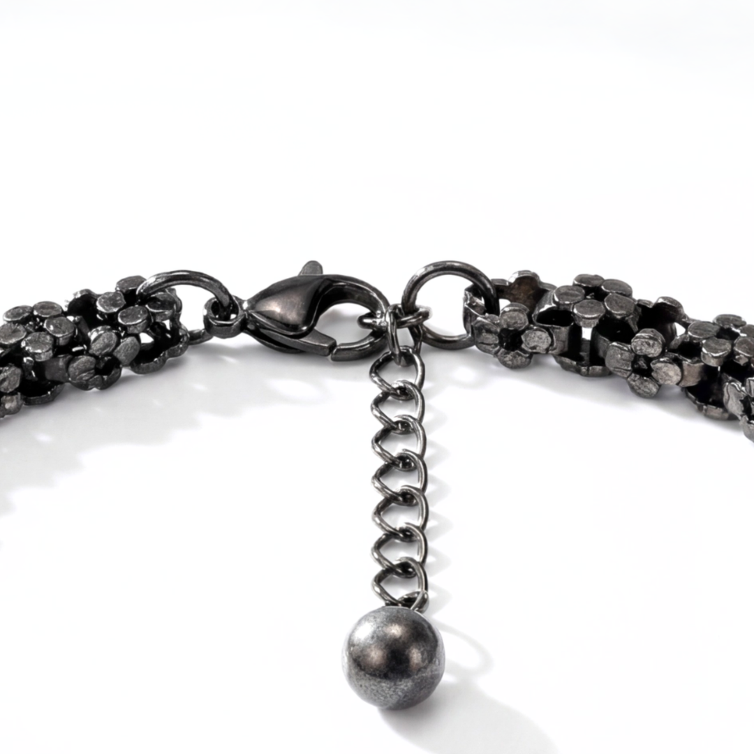 Close-up of a black chain bracelet with a lobster clasp and spherical charm on a white background