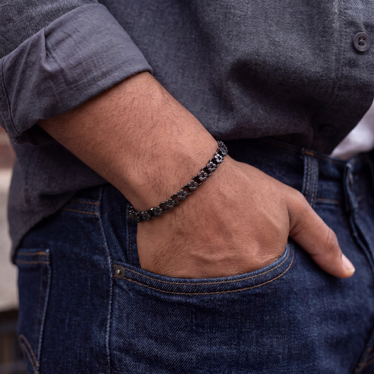 Person wearing a metal floral bracelet on a hand with jeans and a dark shirt.
