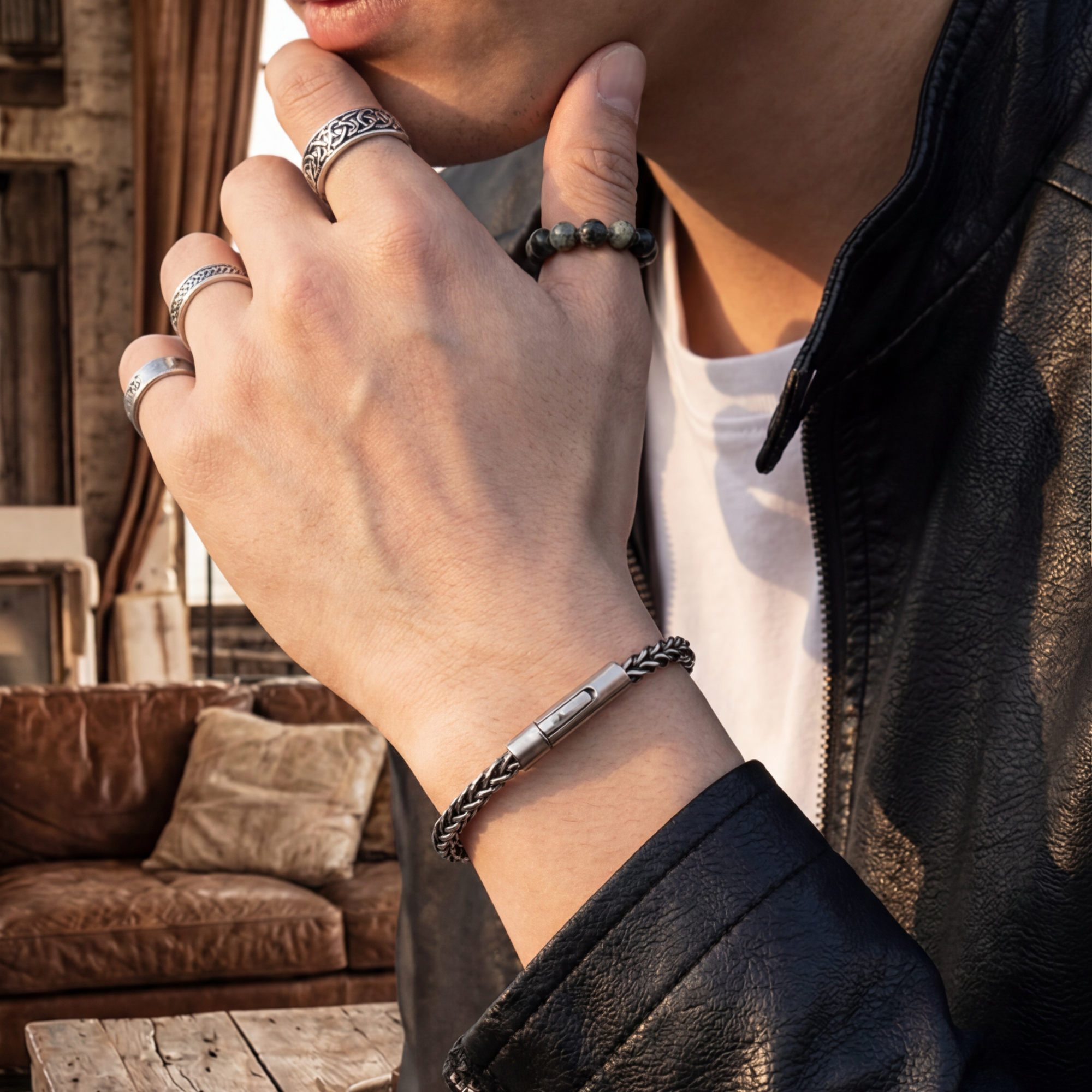 Close-up of a person's hand wearing multiple rings and a bracelet with a blurred indoor background.