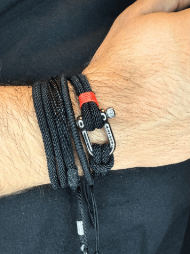Close-up of a wrist wearing a black braided bracelet with a carabiner on a dark background