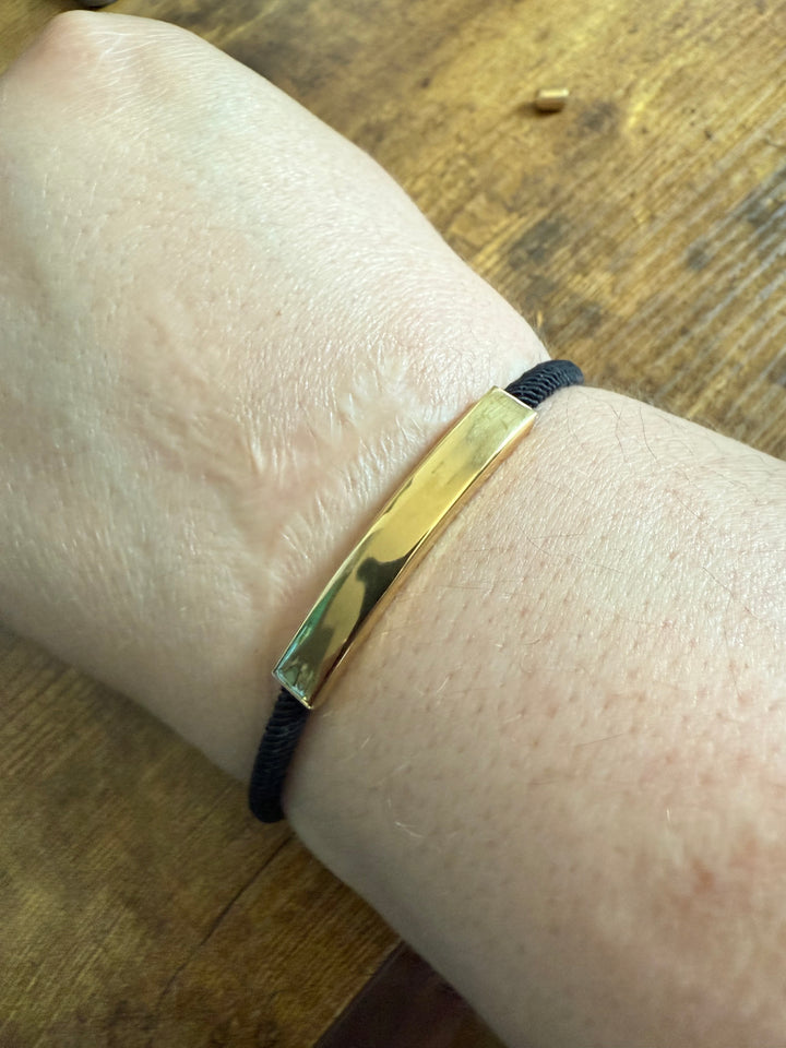 A black and gold rope bracelet on a wrist