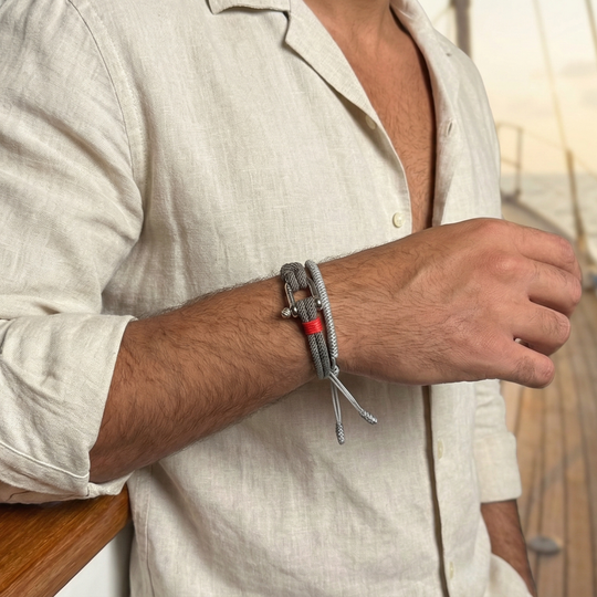 A man wearing a linen shirt with a grey rope bracelet with red binding and a metal clasp 