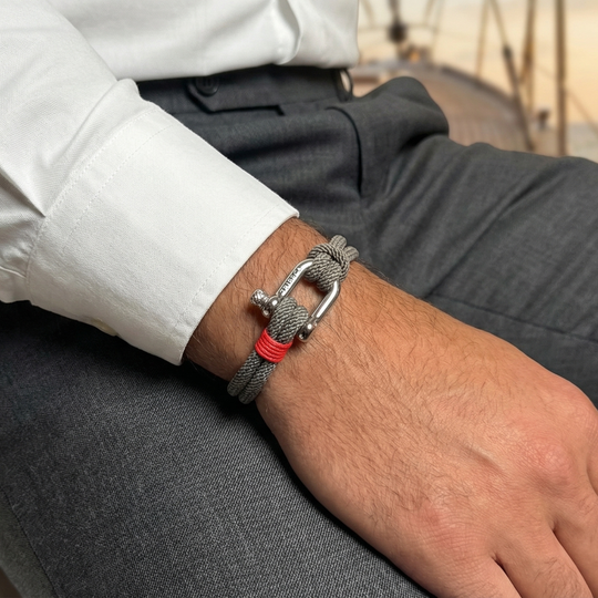 A man wearing dress cloths with a grey rope bracelet with red binding and a metal clasp 