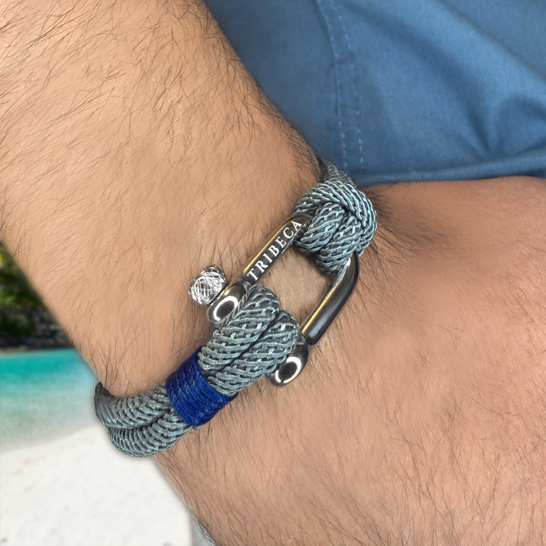 A grey and blue rope bracelet with a metal clasp on a man's wrist 