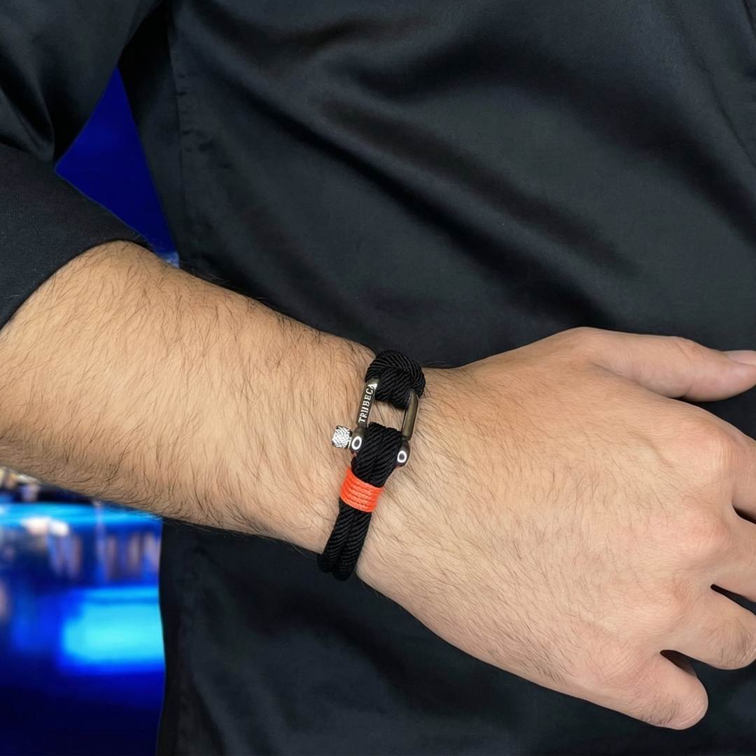 A man wearing a black silk shirt with a black rope bracelet with red binding and a metal clasp