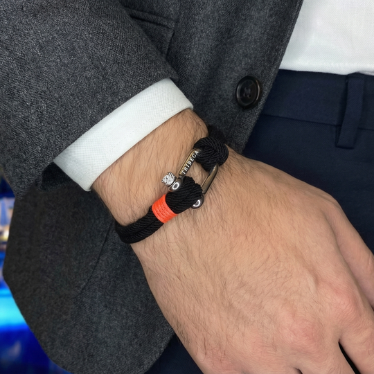 A man wearing dress clothes with a black rope bracelet with red binding and a metal clasp. 