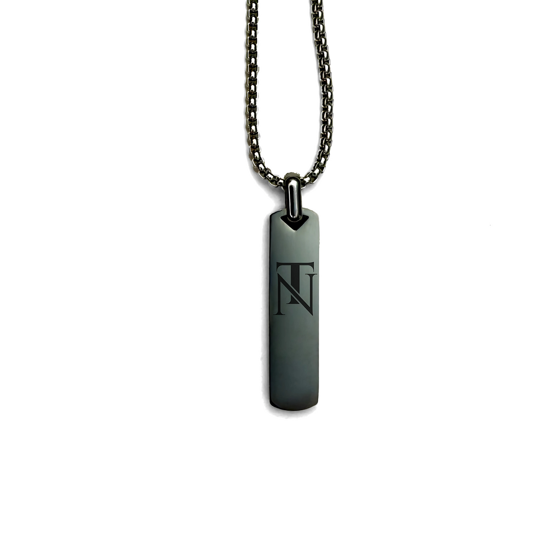 A stainless steel pendant necklace with a rectangular tag featuring the Tribeca Noir Brand's logo, displayed on a chain against a white background.