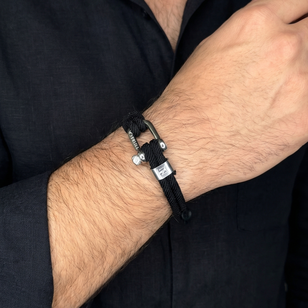 Black bracelet with steel clasp on a wrist against a black shirt background