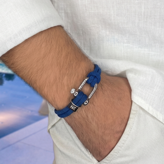 A man wearing white linens and a blue rope bracelet with metal clasps