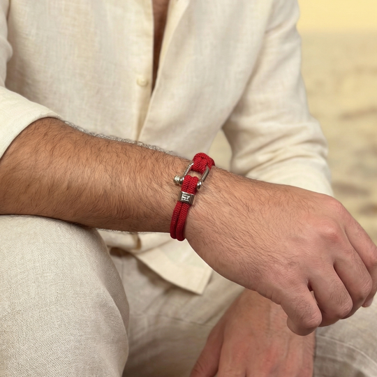 A man wearing light linens and a red rope bracelet with steel clasps
